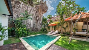 A swimming pool surrounded by lush greenery, a wooden deck, and a small outdoor seating area with a red umbrella. - Tropical Villa Sinar Maluku (Ungasan)