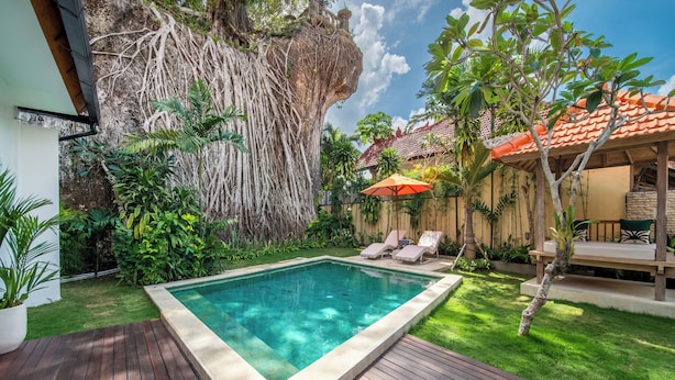 A swimming pool surrounded by lush greenery, a wooden deck, and a small outdoor seating area with a red umbrella. - Tropical Villa Sinar Maluku (Ungasan)