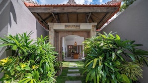 A villa entrance with a stone pathway leading to a wooden table and chairs under a covered area. - Tropical Villa Sinar Maluku (Ungasan)