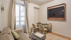 Una sala de estar moderna con un sofá, una mesa de comedor con sillas, un televisor de pantalla plana en la pared y un ventanal con cortinas.