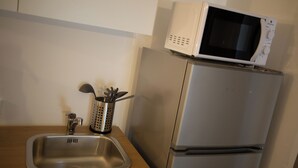 Una cucina con lavello in acciaio inossidabile, un forno a microonde sopra un frigorifero e un portauovelli con cucchiai e spatola.