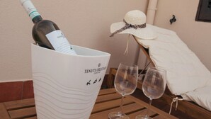 Una bottiglia di vino in un secchio, due bicchieri da vino vuoti e un cappello da sole su un tavolo di legno.
