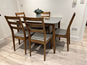 Una mesa de comedor con cuatro sillas de madera, una planta pequeña en maceta y un cuaderno sobre la mesa.