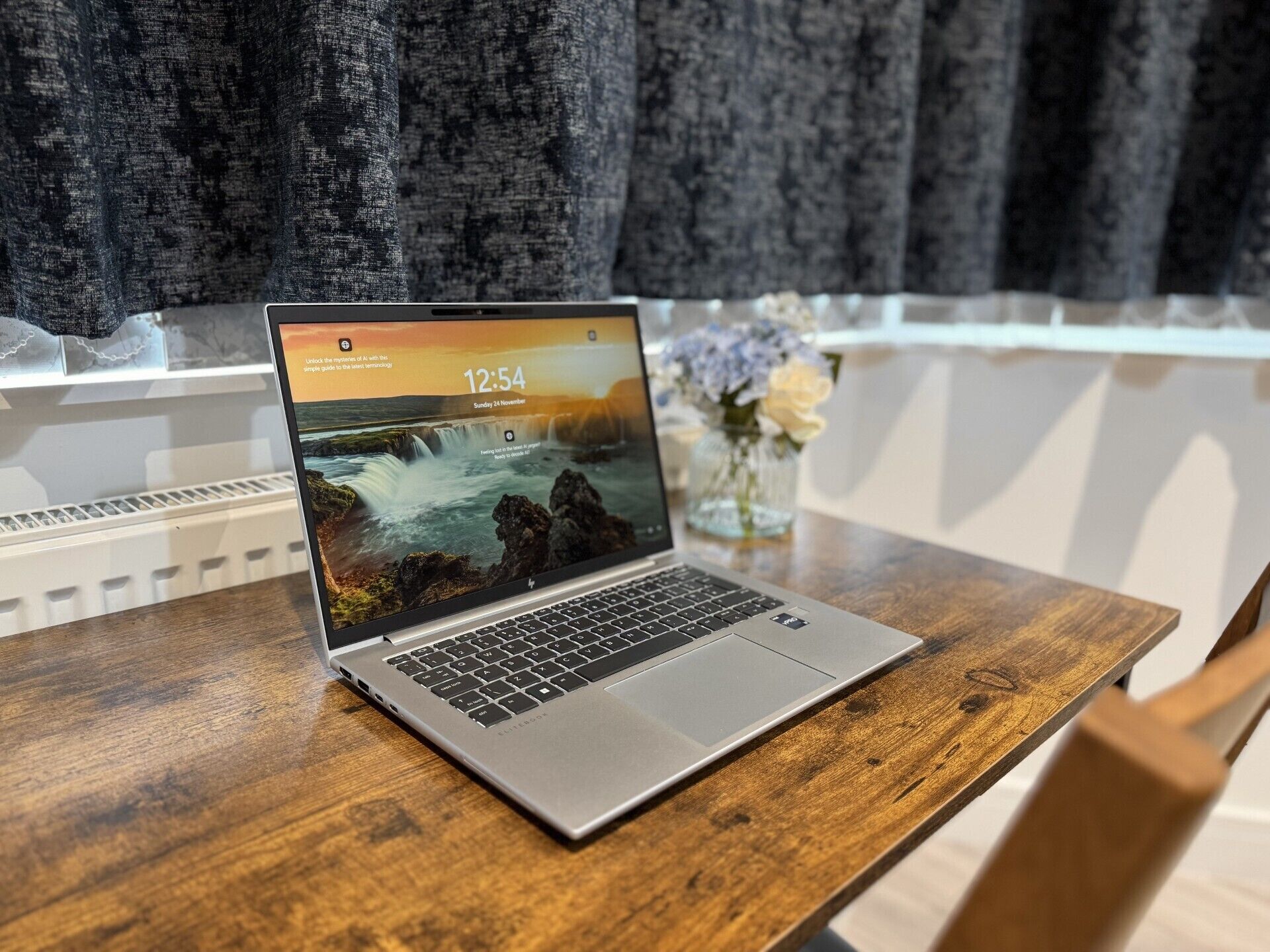 Ein Laptop auf einem Holztisch, im Hintergrund ein dekorativer Wandbelag mit Landschaftsmotiv.