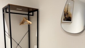A room with a wooden wardrobe, a small wooden table, a white trash bin, and a wall-mounted mirror reflecting an image of the Eiffel Tower. - Deluxe 4 Bedroom House with Free Parking (Slough)