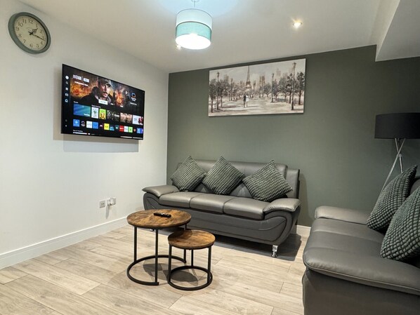 Un salón moderno con un sofá gris, una mesa de centro, un televisor montado en la pared y un cuadro sobre el sofá.