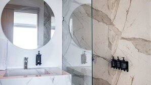 A bathroom with a marble sink, a round mirror, and a glass shower enclosure.