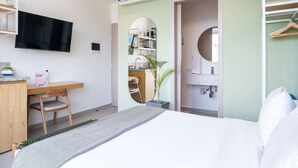 A hotel room with a bed, a desk with a chair, a TV, a mirror, and a wardrobe.