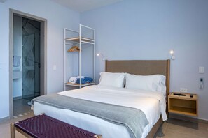 Een keurig opgemaakt hotelkamer met een bed, nachtkastje, kledingkast en een bankje.
