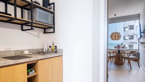 A modern kitchen with wooden cabinets, a granite countertop, and a built-in microwave. There is a dining area with a round table and chairs visible through an open door.