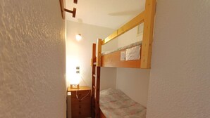 A small, narrow room with a bunk bed, a desk with a chair, and a small cabinet.