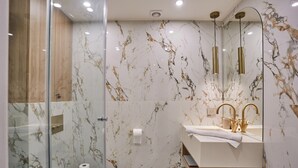 Ein modernes Badezimmer mit Duschkabine aus Glas, Marmorwänden und einem Waschtisch mit goldenem Wasserhahn.