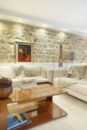 A modern living room with a stone wall, a white sofa, a wooden coffee table, and a lamp. - Superb Terrace Apart Champs Elysees Eiffel Tower (Paris)