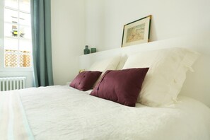 A neatly made bed with white and purple pillows, a framed picture on the wall, and a window with curtains. - Superb Terrace Apart Champs Elysees Eiffel Tower (Paris)