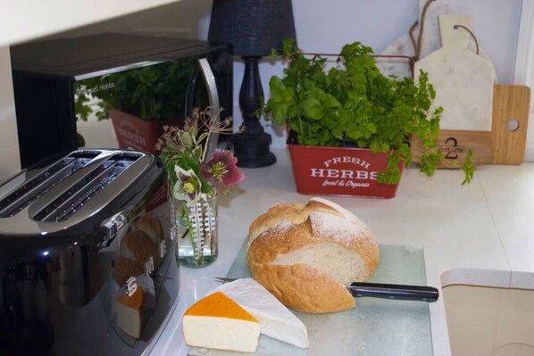 A kitchen counter with a toaster, a loaf of bread, a cheese wedge, and a small vase with flowers. - Quality Country Cottage , Warden, Northumberland. Fishing, Cycling, Walking (Warden)