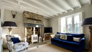 A living room with a stone fireplace, a blue sofa, a floral armchair, and a mounted deer head.