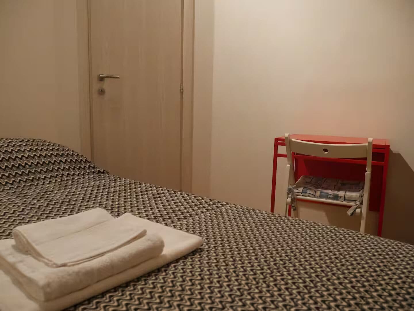 A small room with a bed, a chair, and a door.