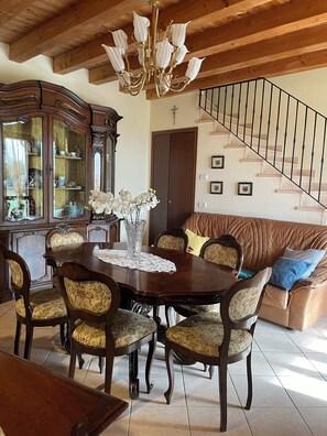 A dining area with a wooden table, chairs, and a chandelier. There is a staircase with a railing and a sofa with cushions. - Villa Rondine is surrounded by nature, close to Garda, Verona and Valpolicella. (Verona)