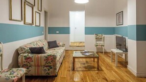A living room with a floral sofa, a glass coffee table, and a television. - Cheerful little house in the heart of the historic center  (Palermo)