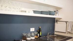 A kitchen with a sink, a shelf with wine glasses and plates, and jars of spices. - Cheerful little house in the heart of the historic center  (Palermo)