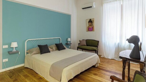 A bedroom with a bed, a chair, a desk, and a painting on the wall. - Cheerful little house in the heart of the historic center  (Palermo)