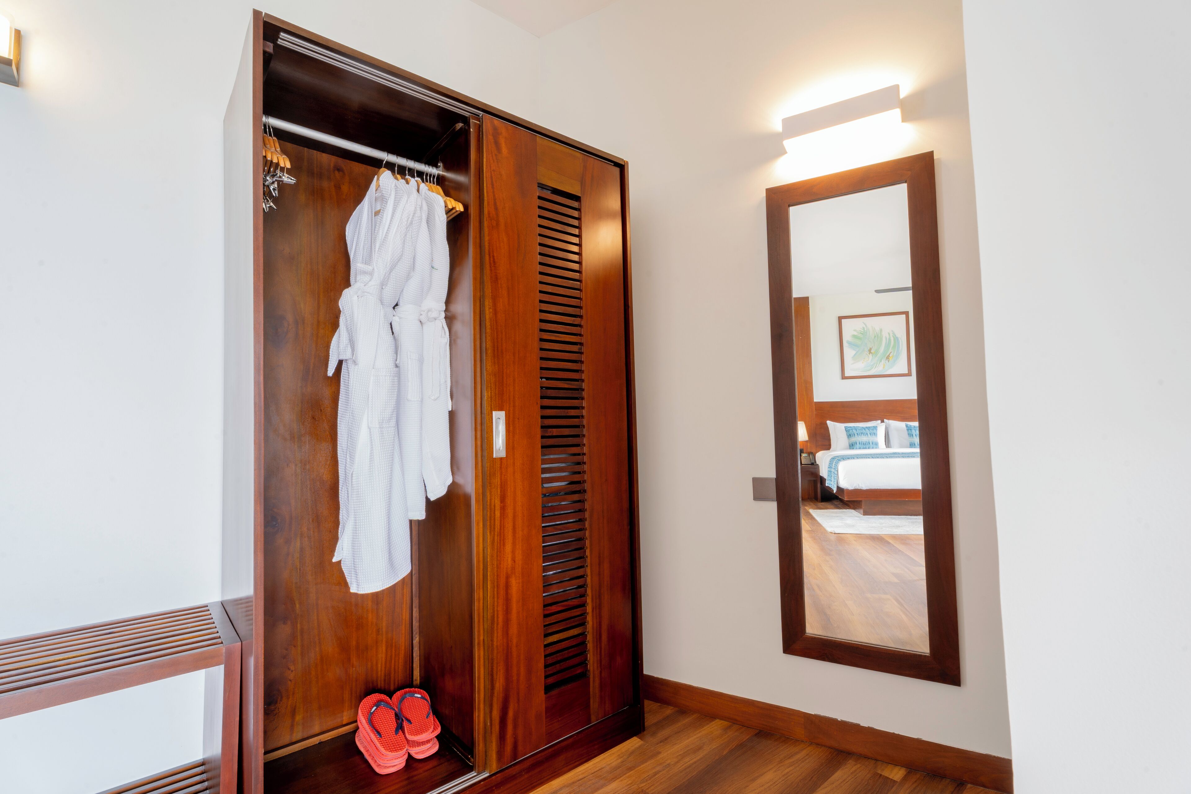 Une armoire en bois avec un miroir, un peignoir suspendu et une paire de tongs.