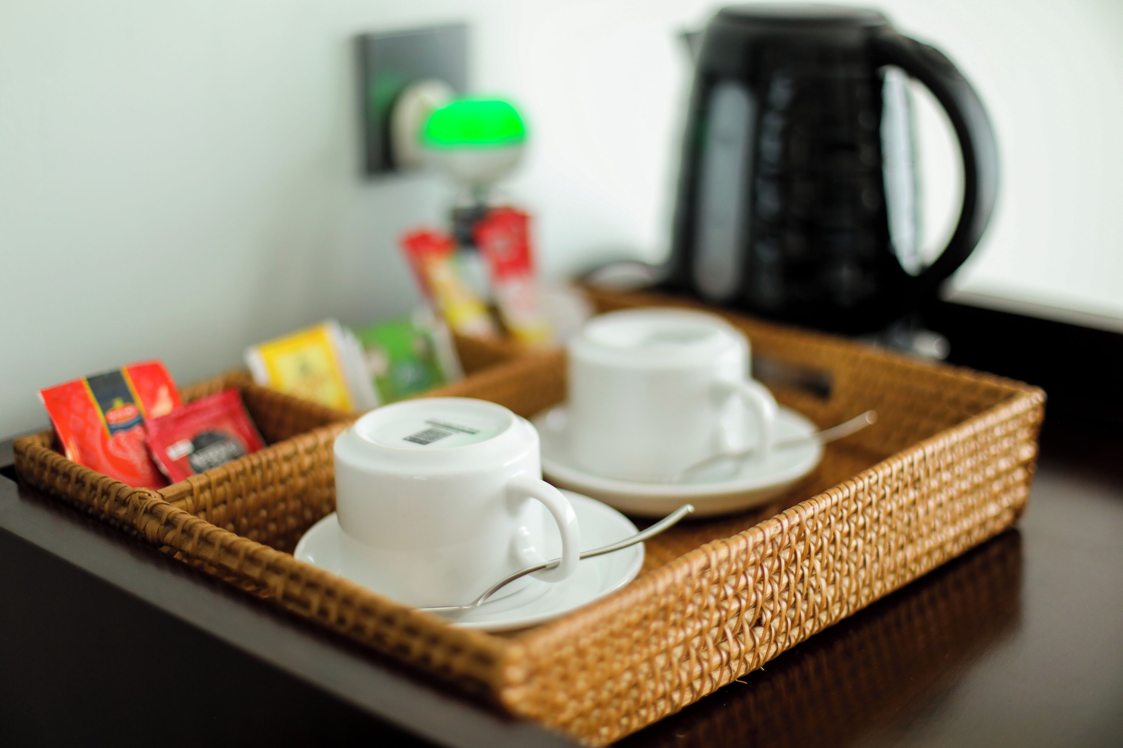 Una bandeja de desayuno con dos tazas y platillos blancos, una cafetera negra y algunos paquetes de comida sobre una mesa de madera oscura.