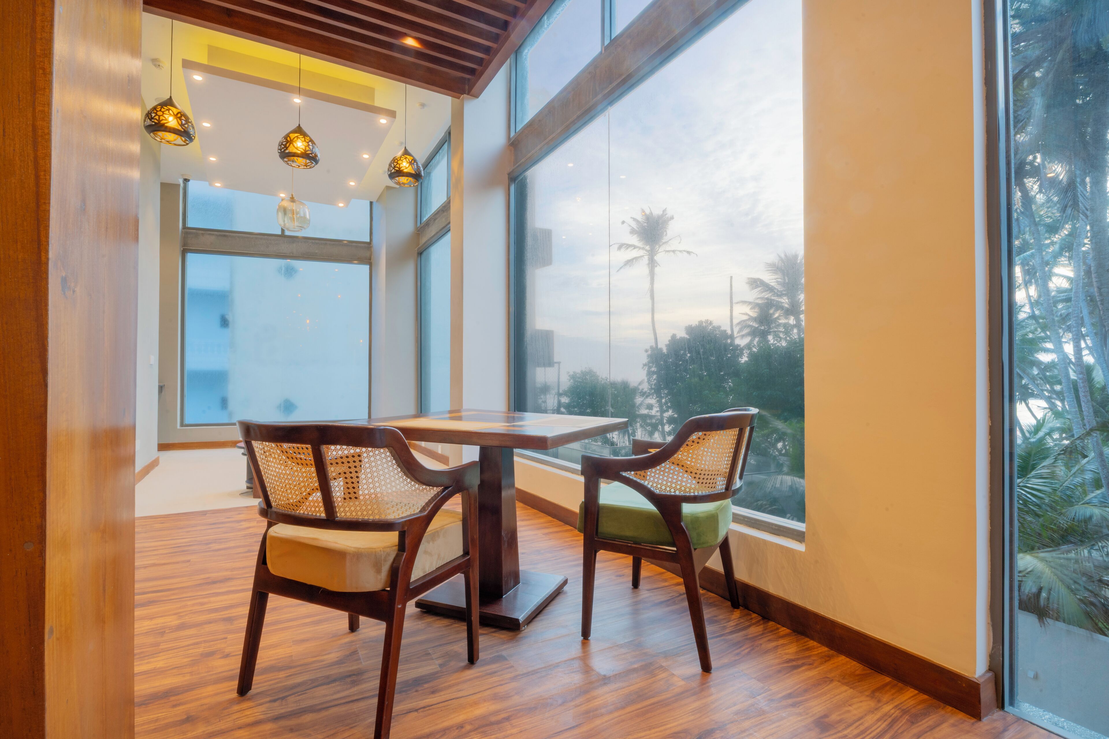A dining area with a wooden table and chairs, large windows, and hanging pendant lights.