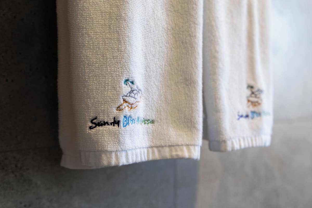 A close-up of a white towel with embroidered text and a small graphic.