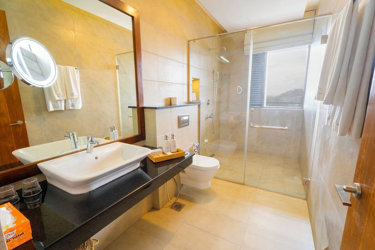 A bathroom with a large mirror, two sinks, a toilet, and a glass-enclosed shower.