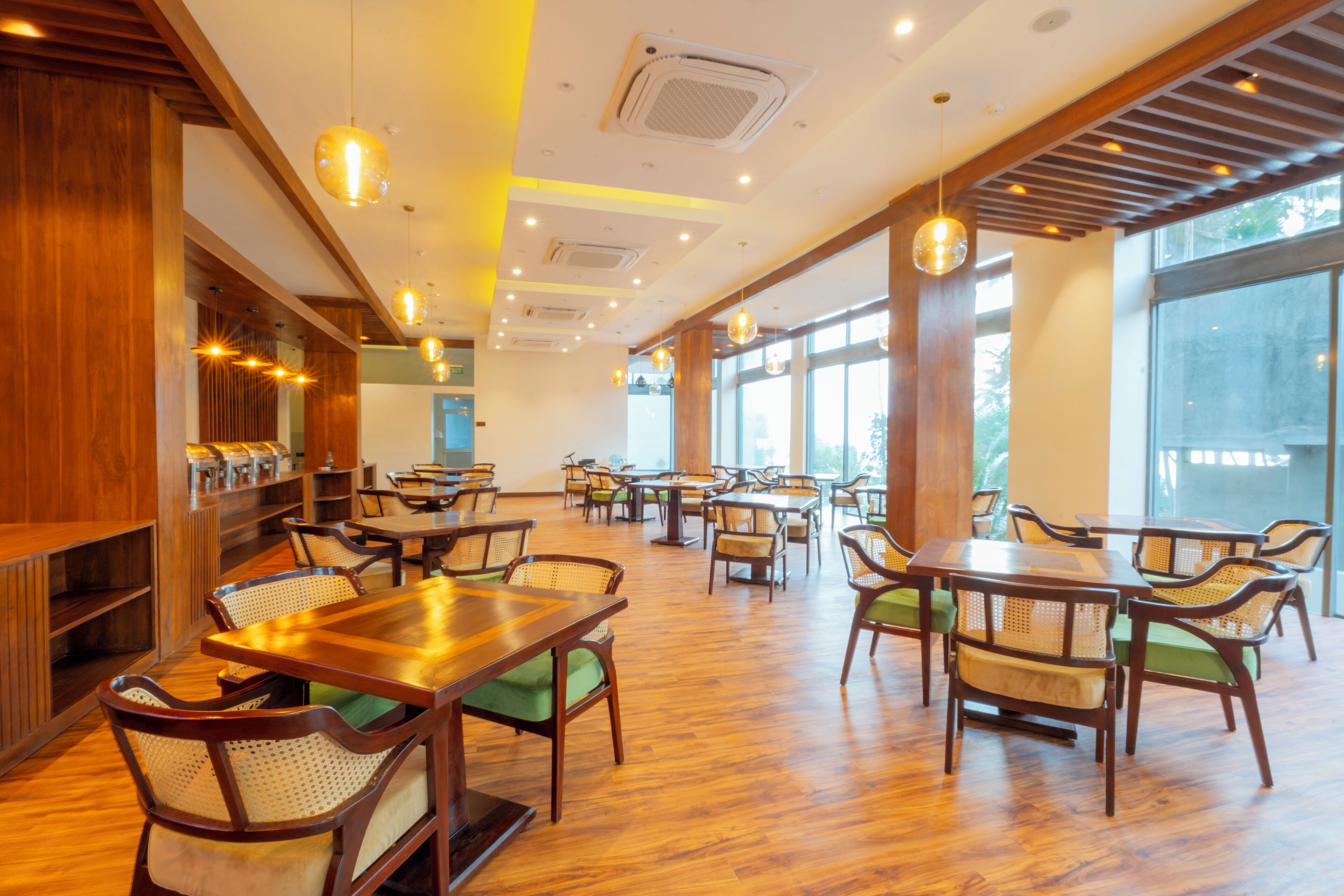 A spacious restaurant with wooden tables and chairs, large windows, and pendant lighting.