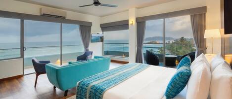 Une chambre d’hôtel avec un grand lit, un fauteuil bleu, une petite table et une vue sur l’océan.