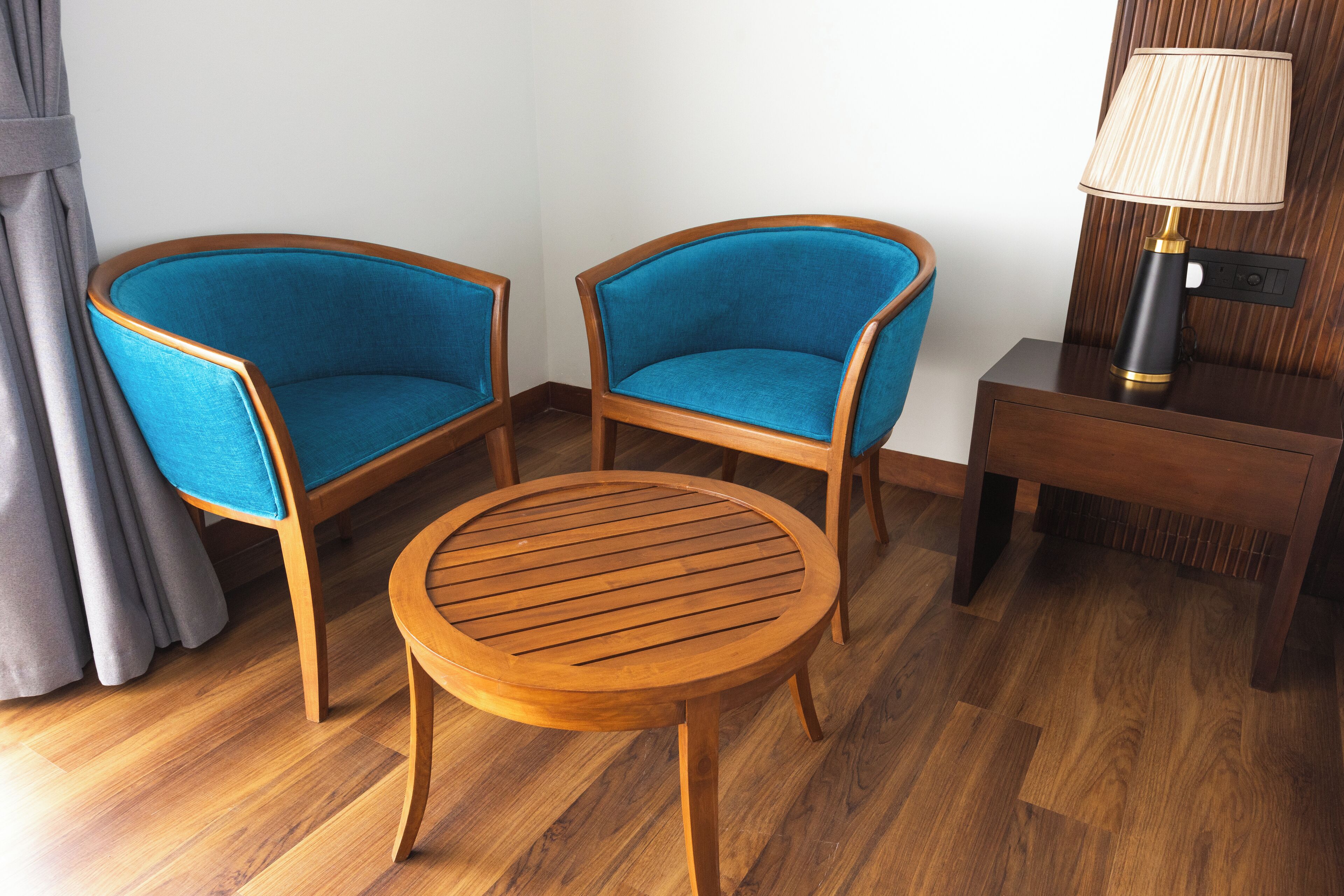 Une pièce d’angle avec deux fauteuils bleus, une table en bois et une table de chevet avec une lampe.