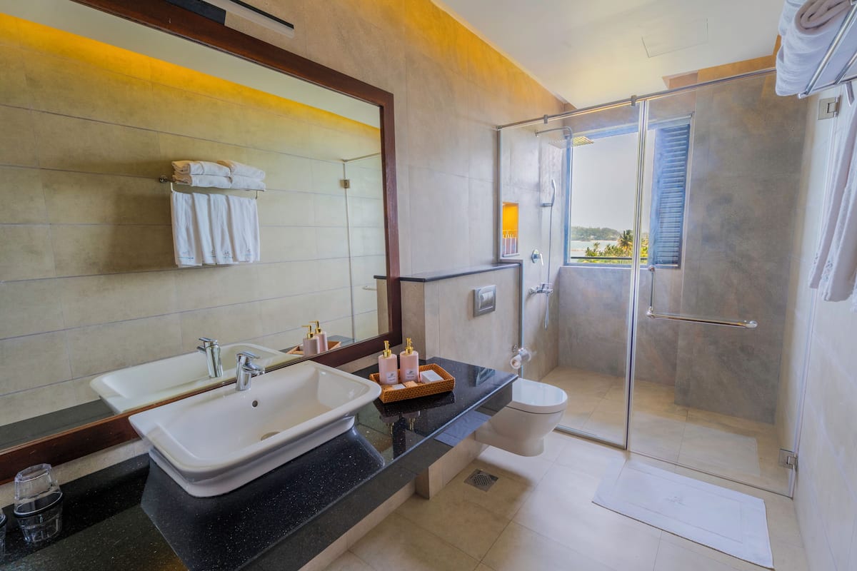 A bathroom with a large mirror, two sinks, a toilet, and a glass-enclosed shower.