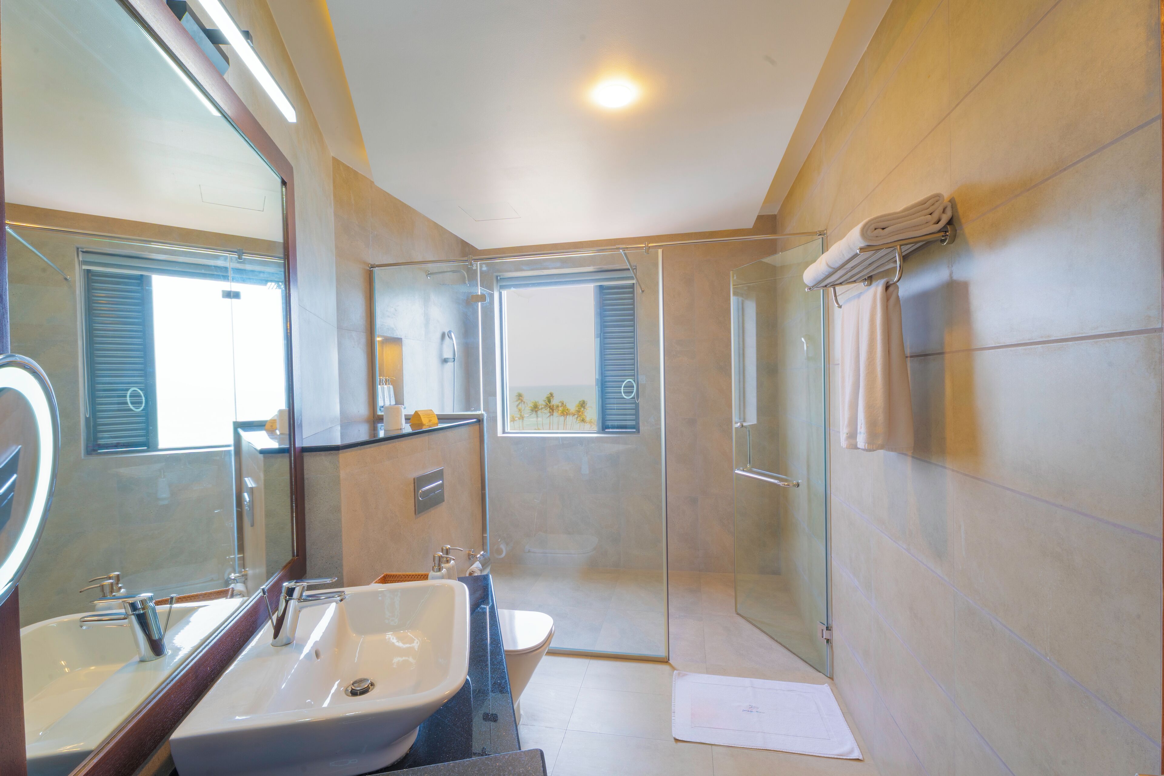 A modern bathroom with a large mirror, two sinks, a toilet, and a glass-enclosed shower.