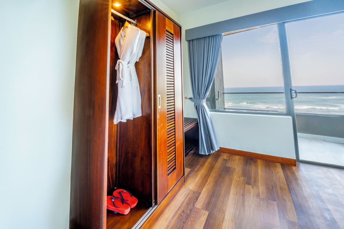 A room with a wooden wardrobe, a pair of red slippers, and a view of the ocean through a balcony with a curtain.