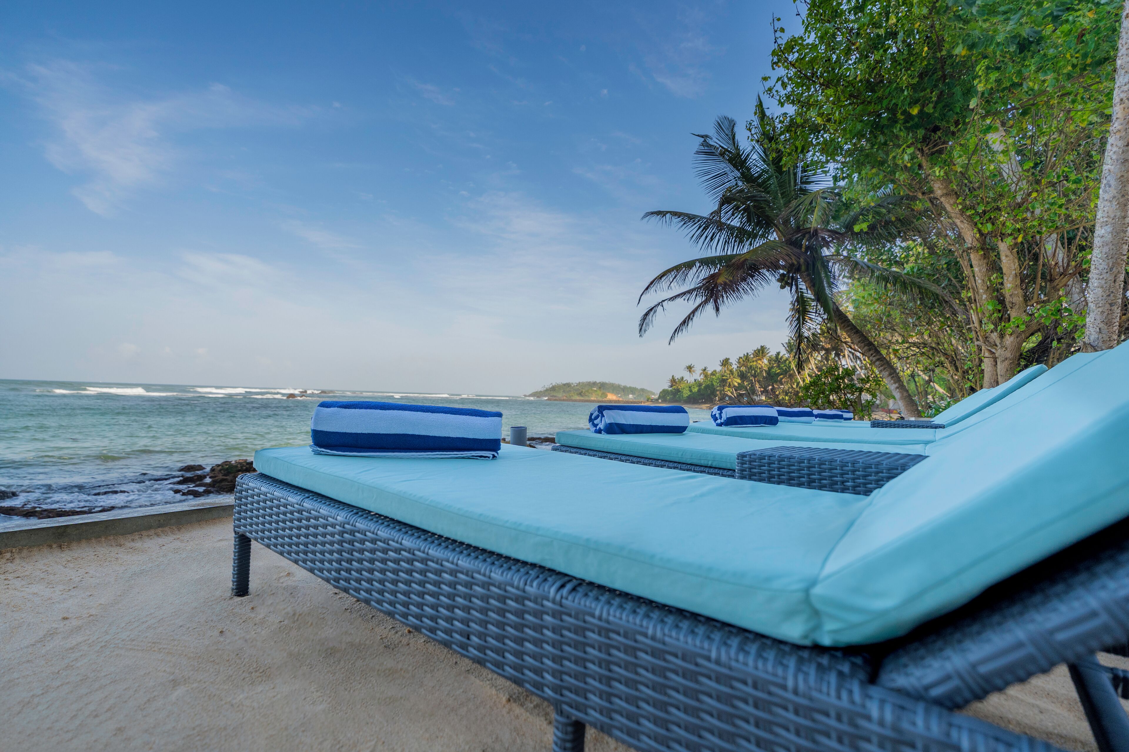 Eine Strandlounge mit Korbmöbeln und hellblauen Kissen mit Blick auf den Ozean.