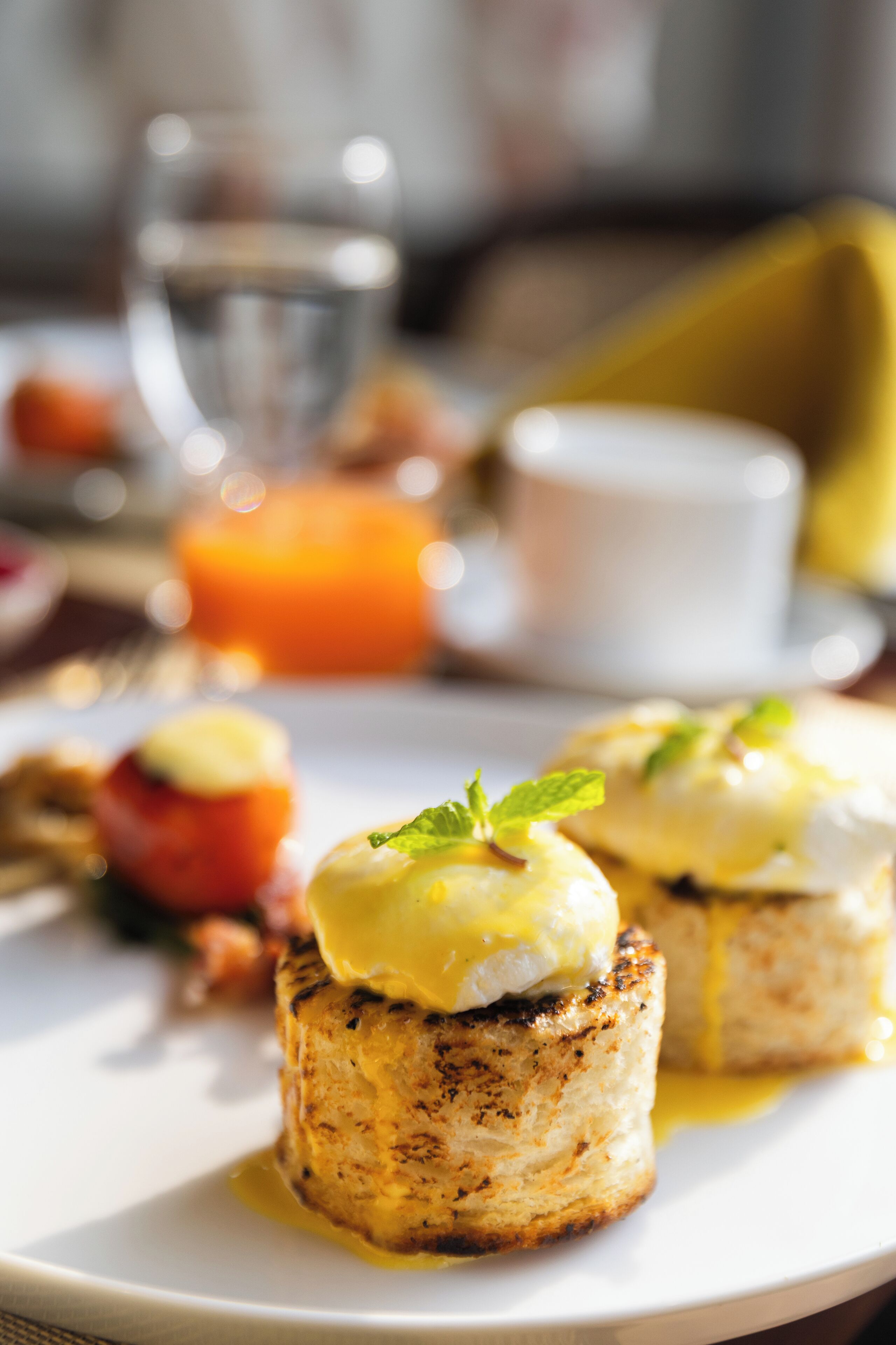 A plate with a grilled item topped with a creamy sauce and a garnish, accompanied by a glass of orange juice and a cup.