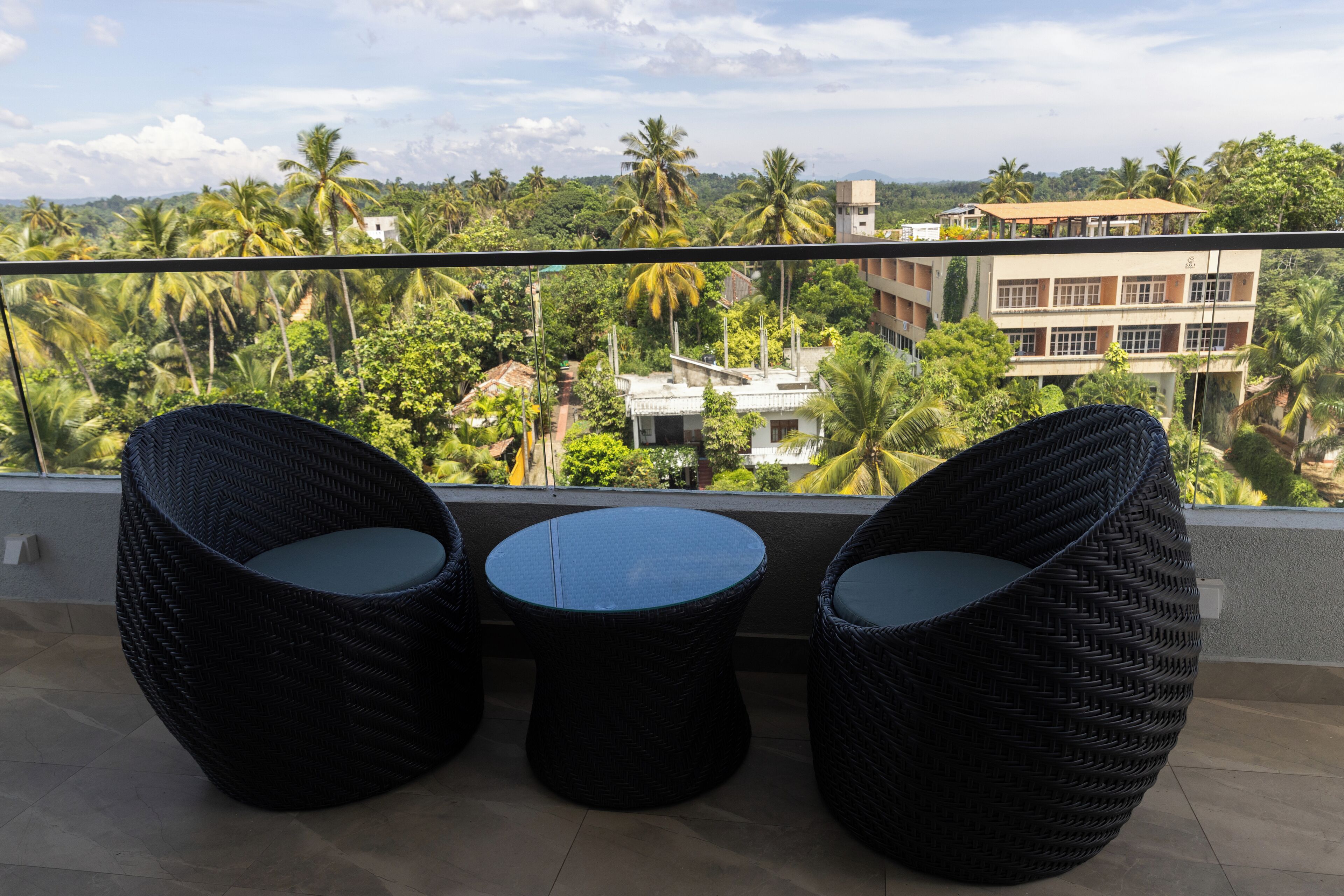 A balcony with wicker furniture and a view of palm trees and buildings.