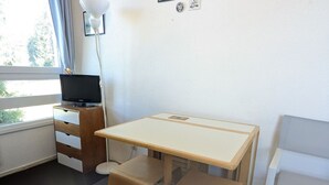 Une petite pièce bien éclairée, avec un bureau, une chaise et un téléviseur.