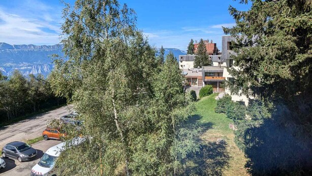 Un bâtiment moderne à plusieurs étages, entouré d’arbres et offrant une vue dégagée sur une chaîne de montagnes.