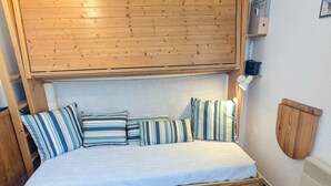 Un lit en bois avec une tête de lit, plusieurs oreillers, une table de chevet et un radiateur fixé au mur.