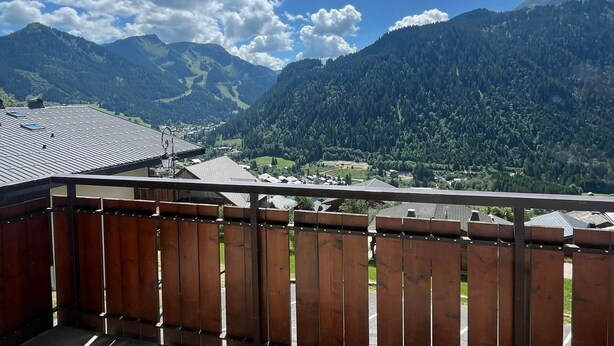 Un balcon offrant une vue sur un paysage montagneux, un village en contrebas et une clôture en bois au premier plan.
