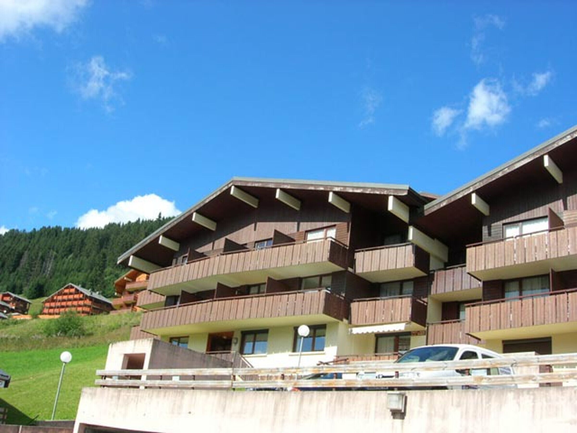 A multi-story building with balconies, likely a hotel or apartment complex, set against a mountainous backdrop.