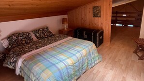 Une chambre à coucher avec un lit, une table de chevet, une lampe, une valise et un plafond en bois.
