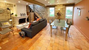 Un salon chaleureux avec une cheminée, un canapé, une table à manger avec des chaises et un escalier menant à l’étage supérieur.