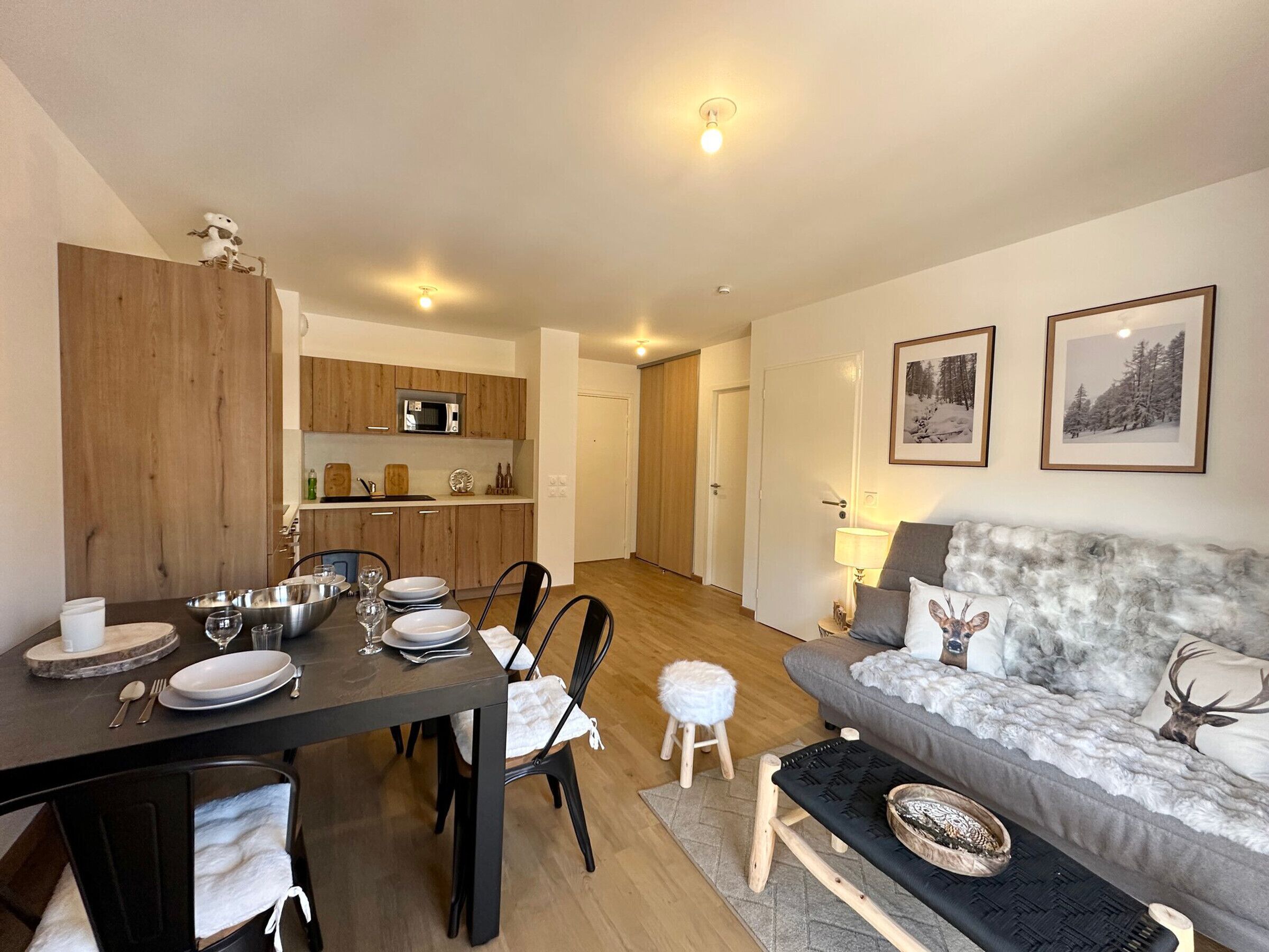 A modern living room with a grey sofa, a dining table set for four, and a kitchen in the background.