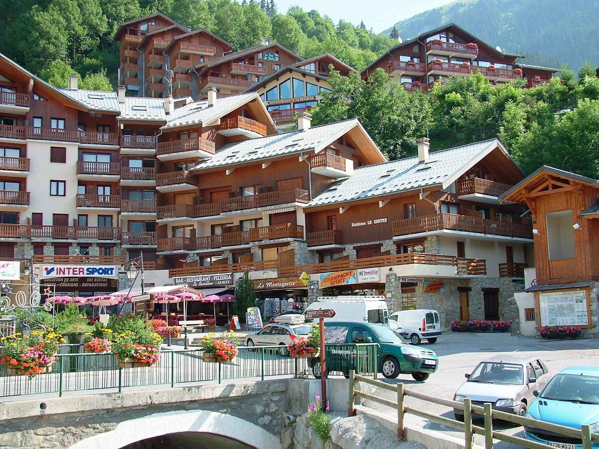 A cluster of wooden buildings with balconies, a sign for 'INTER SPORT', and a 'BAR RESTAURANT - PIZZERIA' sign.