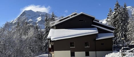 A multi-story building with a sloped roof, surrounded by snow-covered trees and mountains.