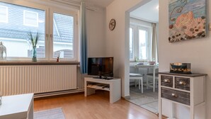 A modern living room with a TV, white furniture, a radiator, and a view of the outside. - Ferienwohnung in Busum (Büsum)